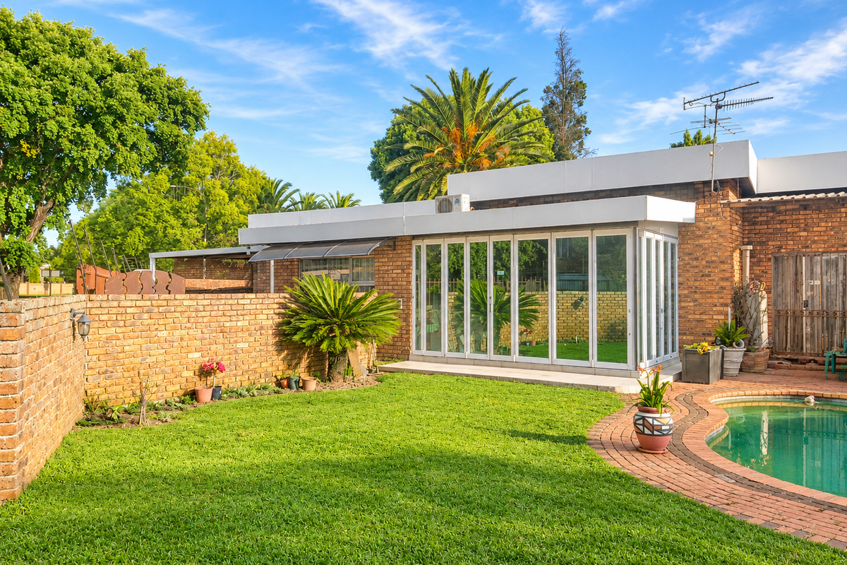Rear view of the property featuring a well-maintained lawn, swimming pool with brick surround, and a modern extension with folding glass doors.