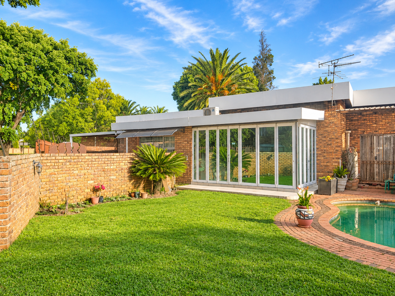 Rear view of the property featuring a well-maintained lawn, swimming pool with brick surround, and a modern extension with folding glass doors.