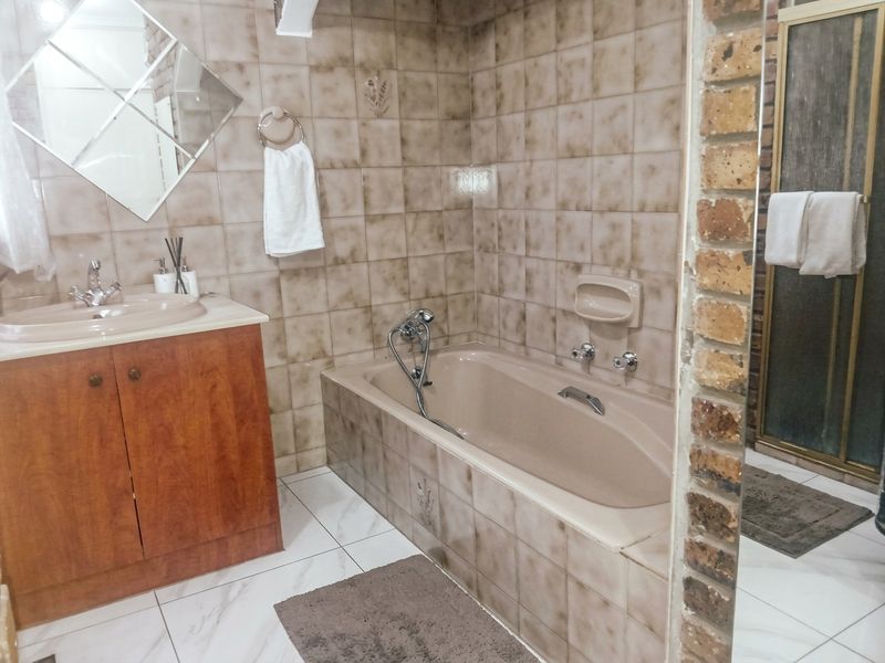 A functional bathroom featuring a built-in vanity, bathtub, and separate shower enclosure with dated ceramic tiling and an exposed brick feature wall.