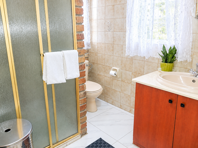A functional bathroom featuring a shower enclosure, toilet, and vanity cabinet with a washbasin, finished with tiled walls and flooring and exposed brick accents.