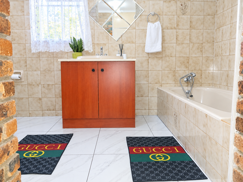 A functional bathroom featuring a vanity cabinet with a ceramic basin, a built-in bathtub with wall-mounted fixtures, and neutral wall and floor tiling.