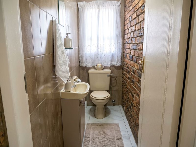Compact bathroom featuring a toilet, vanity basin, tiled walls, and a distinctive exposed brick feature wall.