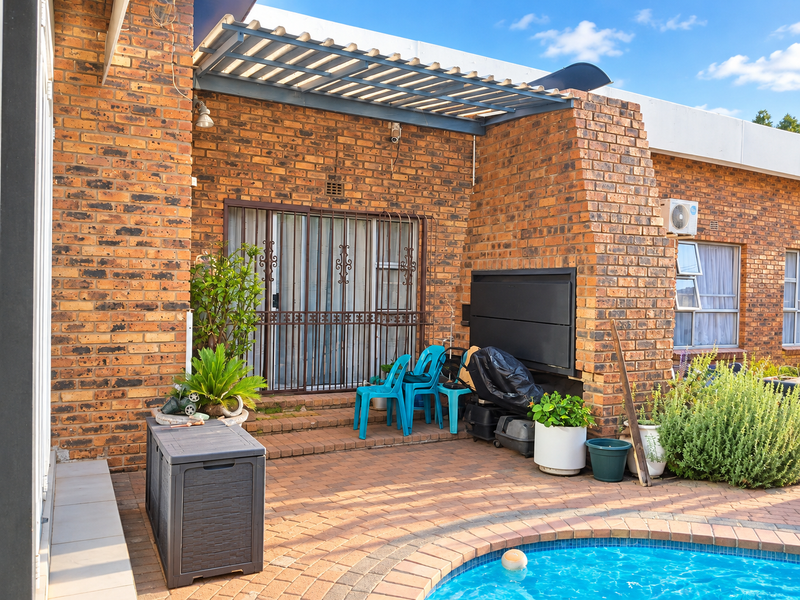 Outdoor pool area featuring a paved patio, built-in braai, and a pergola, providing a functional space for outdoor entertainment and relaxation.