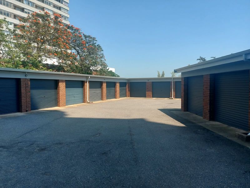 A row of secure lock-up garages with roller shutter doors and brick pillars, situated in a paved courtyard area.