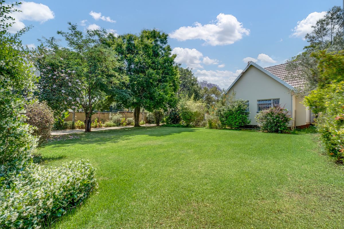 A well-maintained rear garden featuring a spacious lawn, mature trees, and a view of the property's rear elevation with tiled roofing.