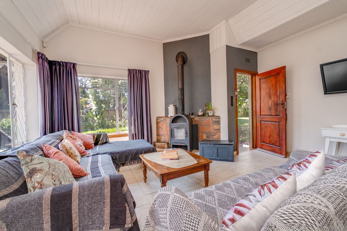 A cozy living room featuring a freestanding fireplace with a stone surround, tiled flooring, and a vaulted ceiling with direct access to the garden.