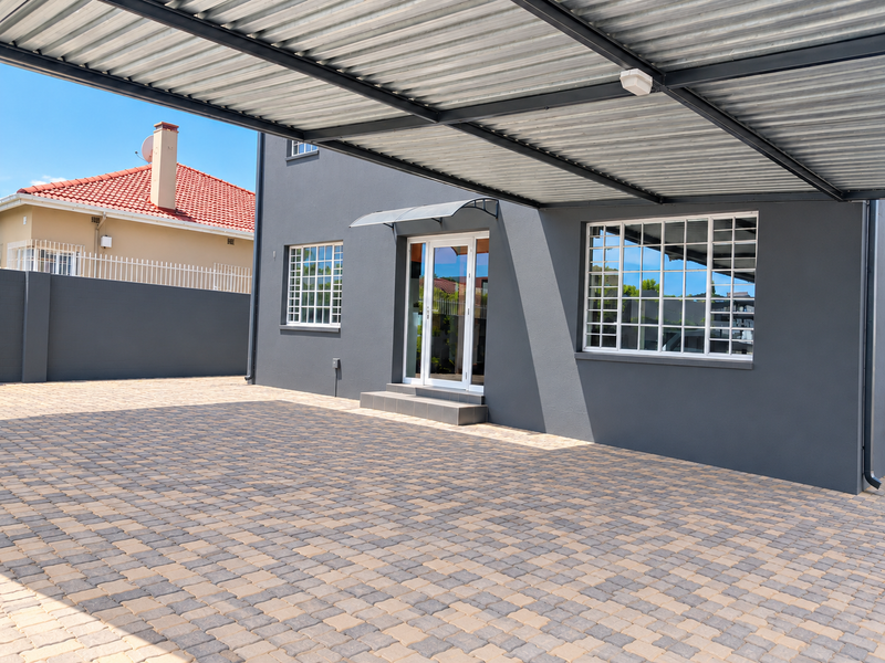 Modern exterior view featuring a spacious paved driveway, a large metal carport, and a well-maintained dark grey facade with grid-pattern windows.