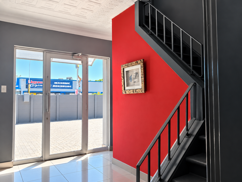 A bright and modern entrance hall featuring a striking red accent wall, a sleek staircase with metal railings, and polished tiled flooring.