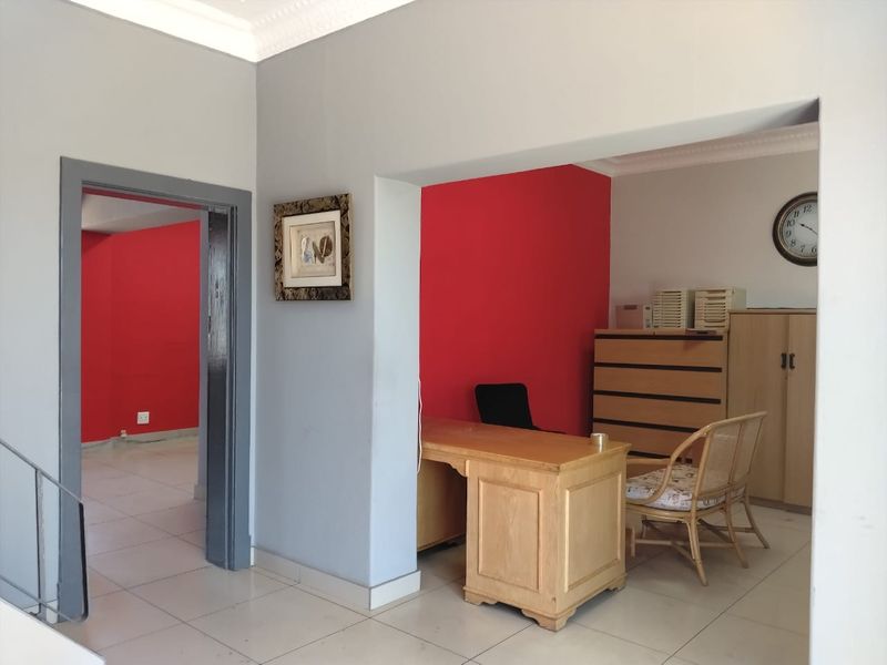A functional office space featuring tiled flooring and decorative ceiling cornices, with an open-plan layout connecting to an adjacent room.