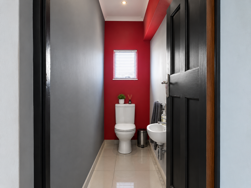 A compact guest bathroom featuring a modern toilet, wall-mounted basin, tiled flooring, and a bold red accent wall.