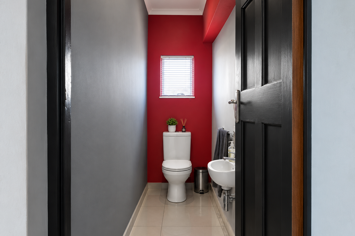 A compact guest bathroom featuring a modern toilet, wall-mounted basin, tiled flooring, and a bold red accent wall.