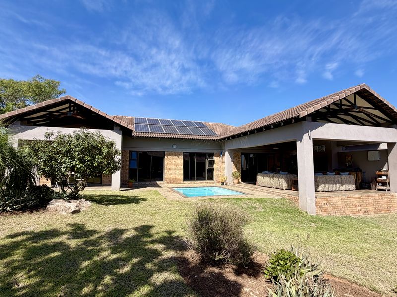 Rear view of the property featuring a spacious covered patio, a swimming pool, and solar panels installed on the tiled roof.