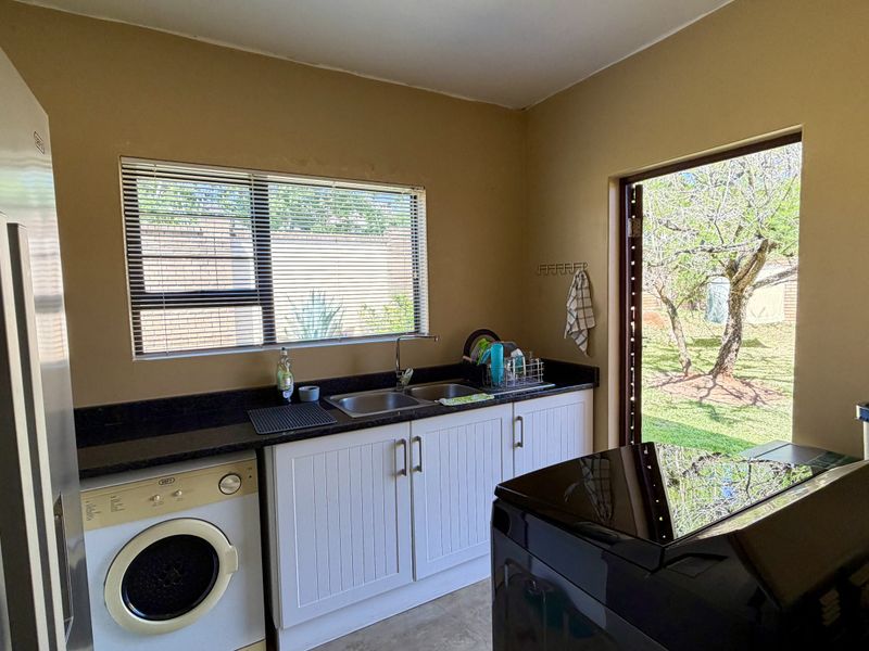 Functional laundry room featuring built-in cabinetry, granite countertops, a double basin sink, and direct access to the rear garden.