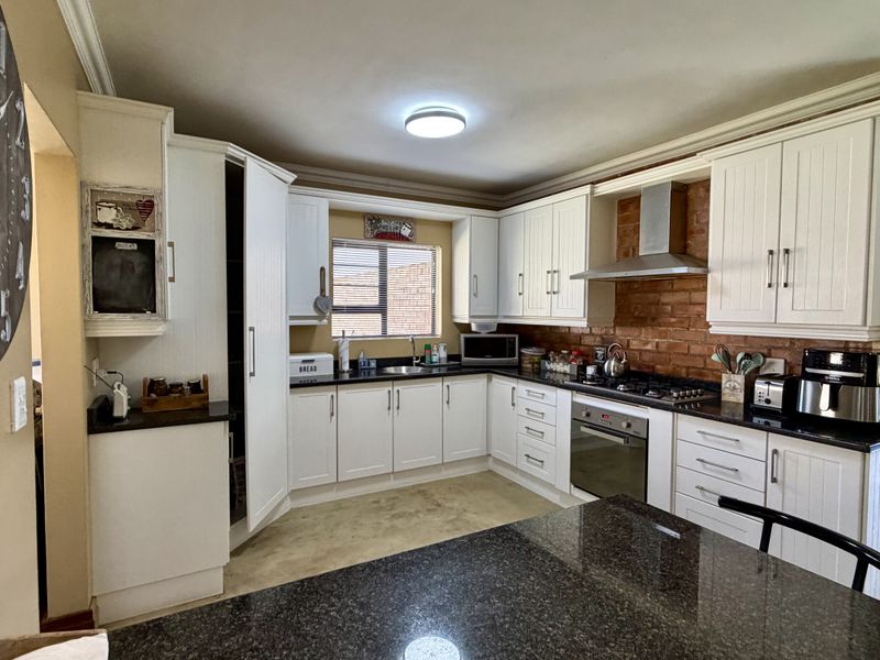 A well-appointed kitchen featuring white cabinetry, granite countertops, an exposed brick splashback, and a central island, offering a blend of classic and industrial styles.