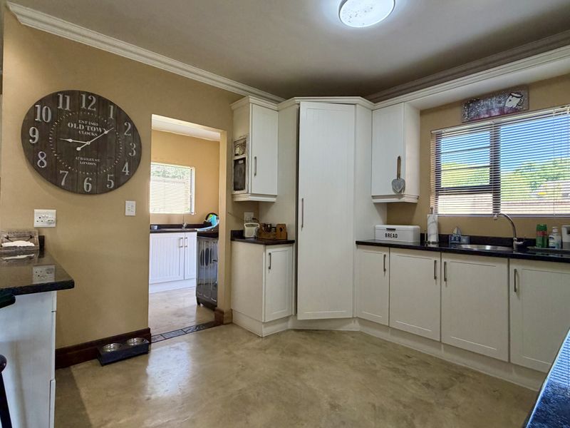 A functional kitchen featuring white cabinetry, dark granite countertops, built-in appliances, and a view through to an adjacent scullery area.