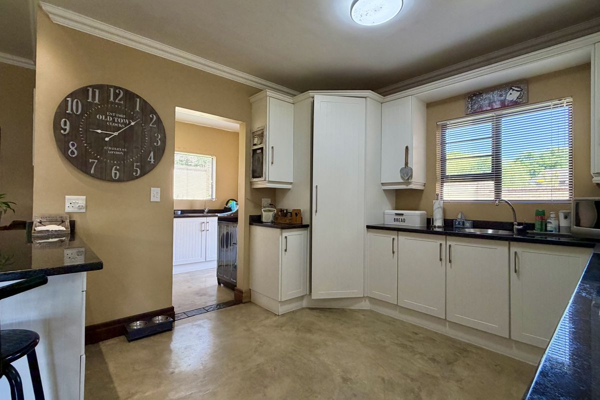 A functional kitchen featuring white cabinetry, dark granite countertops, built-in appliances, and a view through to an adjacent scullery area.