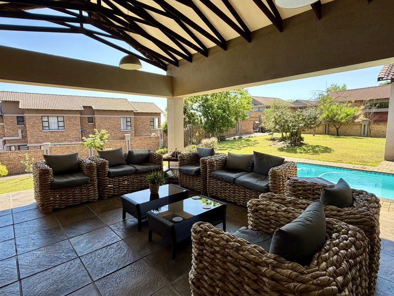 Spacious covered patio featuring tiled flooring and exposed timber trusses, overlooking a private swimming pool and well-maintained garden area.