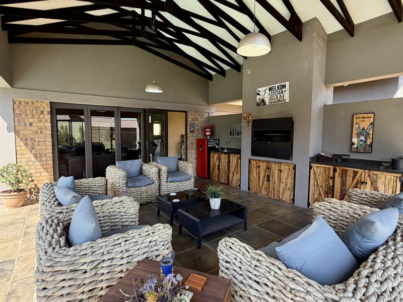 Spacious covered patio featuring a built-in braai, custom cabinetry, exposed timber rafters, and direct access to the home through large sliding glass doors.