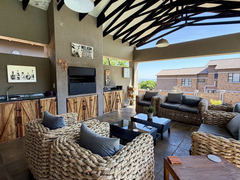 Covered outdoor patio featuring a built-in braai, stone-topped prep area with sink, timber cabinetry, and exposed rafter ceiling, ideal for alfresco entertaining.