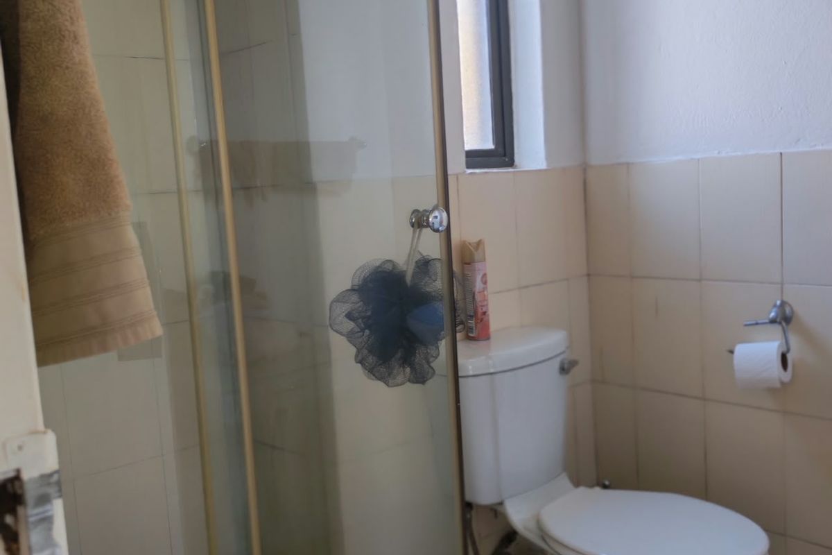 A compact bathroom featuring a shower enclosure, toilet, and tiled finishes, requiring some maintenance to the door frame and tiling.