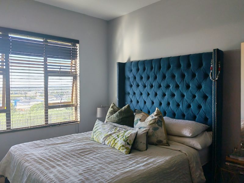 A well-lit bedroom featuring a large window with venetian blinds, offering natural light and an elevated view.