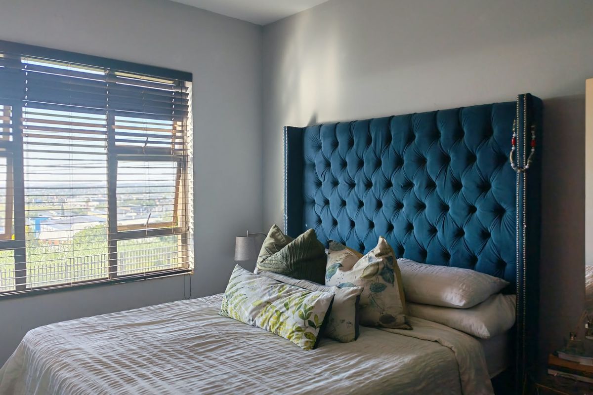 A well-lit bedroom featuring a large window with venetian blinds, offering natural light and an elevated view.