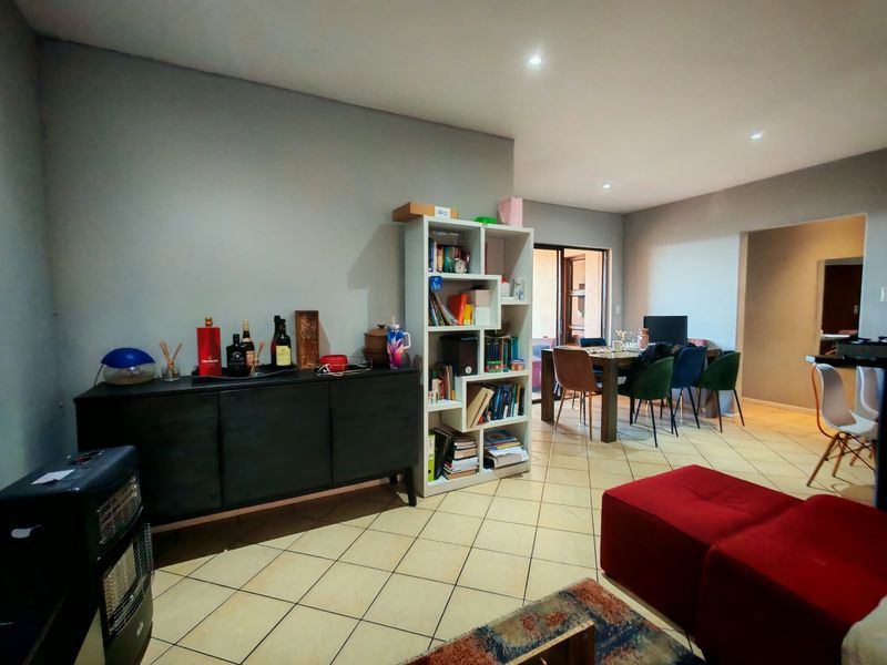 An open-plan living and dining area featuring neutral wall tones, recessed downlighting, and tiled flooring throughout the space.