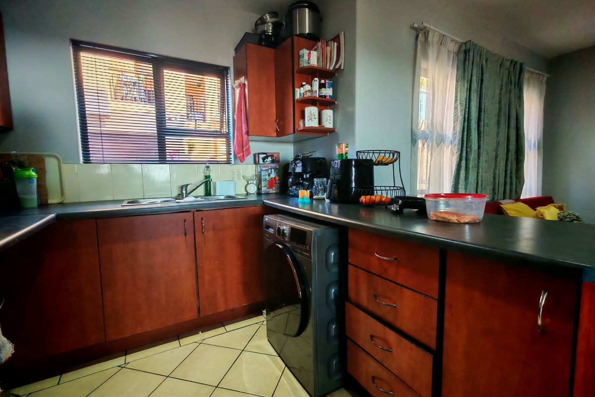 Functional kitchen featuring wood-finish cabinetry, dark laminate countertops, tiled flooring, and a built-in sink area with integrated laundry appliance space.