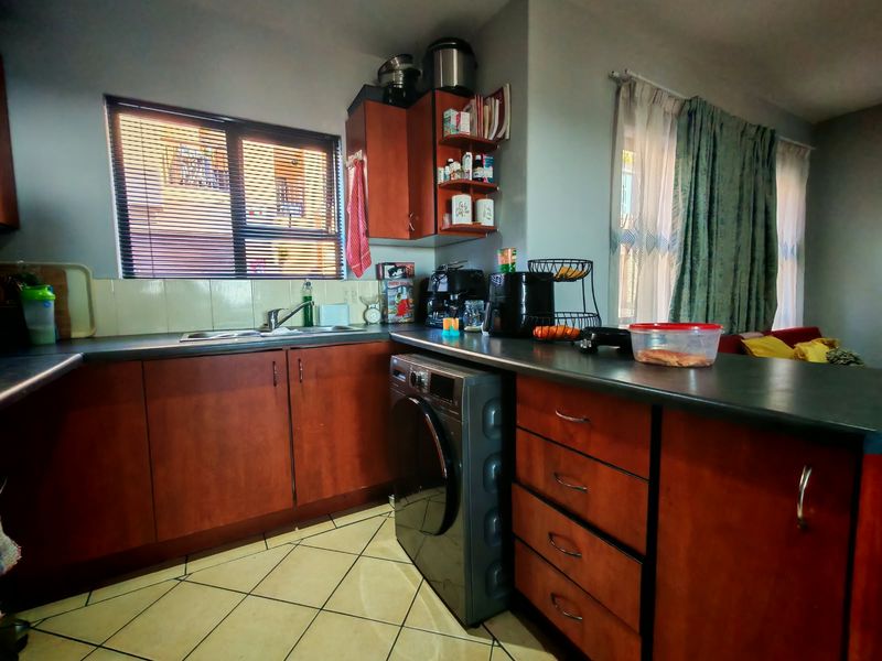 Functional kitchen featuring wood-finish cabinetry, dark laminate countertops, tiled flooring, and a built-in sink area with integrated laundry appliance space.