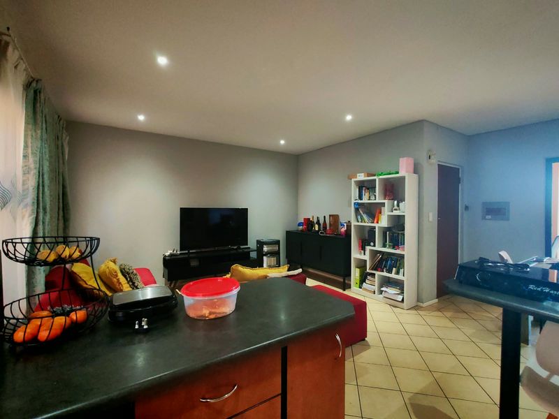 An open-plan living area featuring tiled flooring, recessed downlighting, and a functional kitchen island, creating a versatile space for daily living and entertaining.