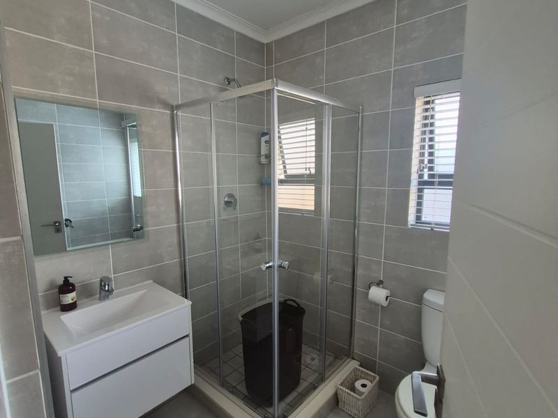 A modern, well-maintained bathroom featuring a glass shower enclosure, wall-mounted vanity with basin, and neutral grey floor-to-ceiling tiling.