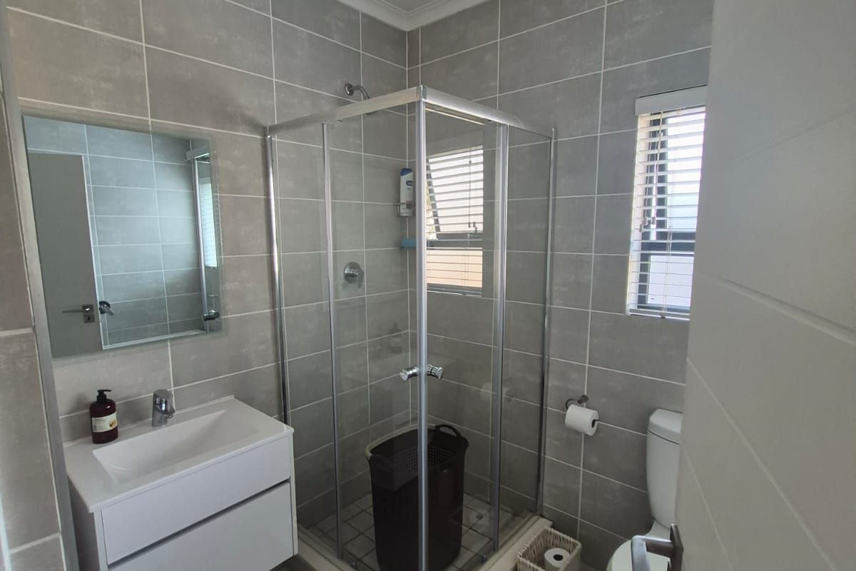 A modern, well-maintained bathroom featuring a glass shower enclosure, wall-mounted vanity with basin, and neutral grey floor-to-ceiling tiling.