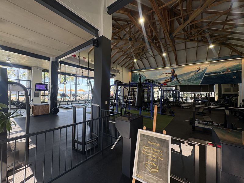 Spacious, well-equipped gym featuring exposed timber roof trusses, large windows, and durable rubberized flooring in a modern, open-plan layout.