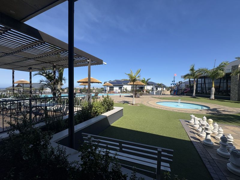 A well-maintained outdoor leisure area featuring a swimming pool, covered pergola, artificial lawn, and landscaped garden space.