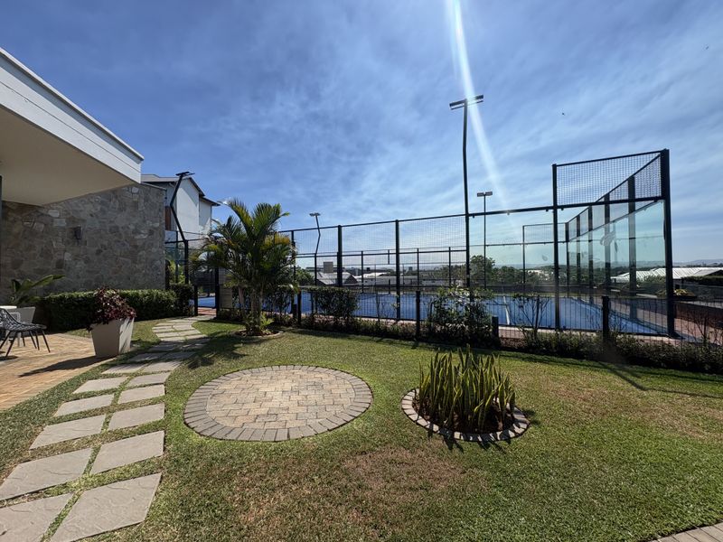 Well-maintained outdoor area featuring a private padel court with floodlights, adjacent to a landscaped garden with stone-clad building exterior and paved walkways.