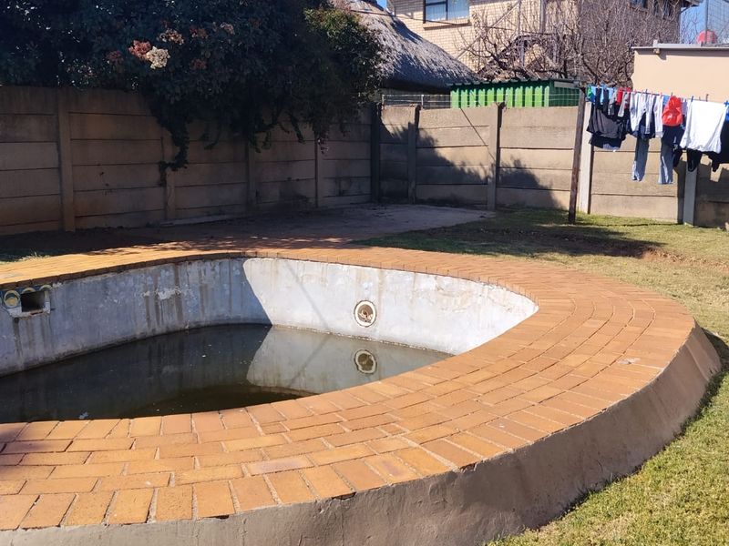 Outdoor pool area featuring a brick-edged swimming pool set within a garden with precast concrete boundary walls.