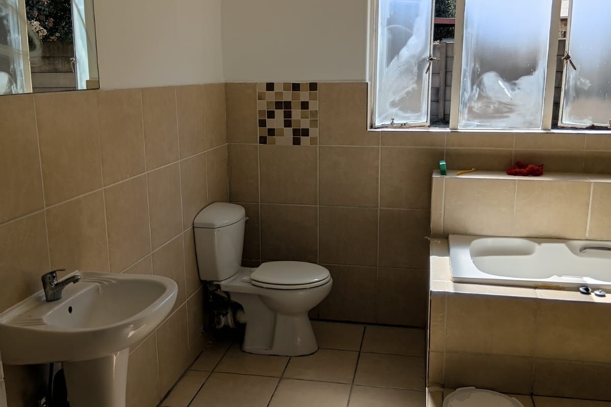 A functional bathroom featuring a pedestal basin, toilet, and a built-in bathtub with tiled surround and flooring.