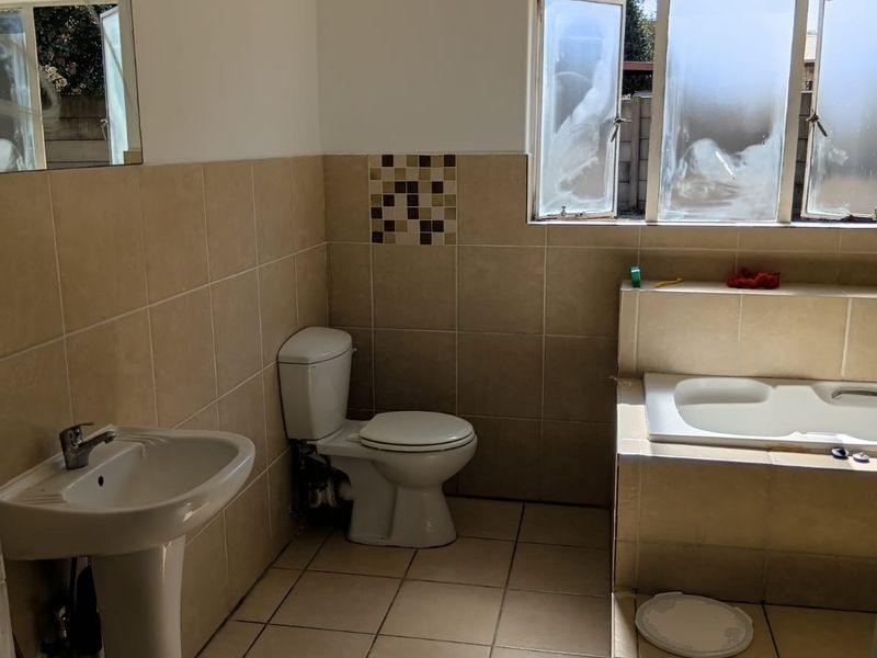 A functional bathroom featuring a pedestal basin, toilet, and a built-in bathtub with tiled surround and flooring.