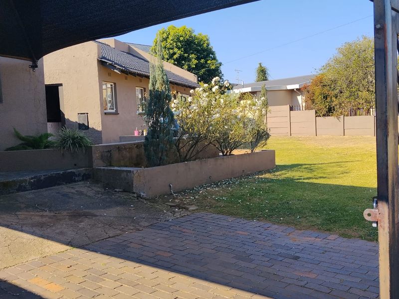 Rear exterior view featuring a paved patio area, shade sail, and a raised garden bed set against the house structure.