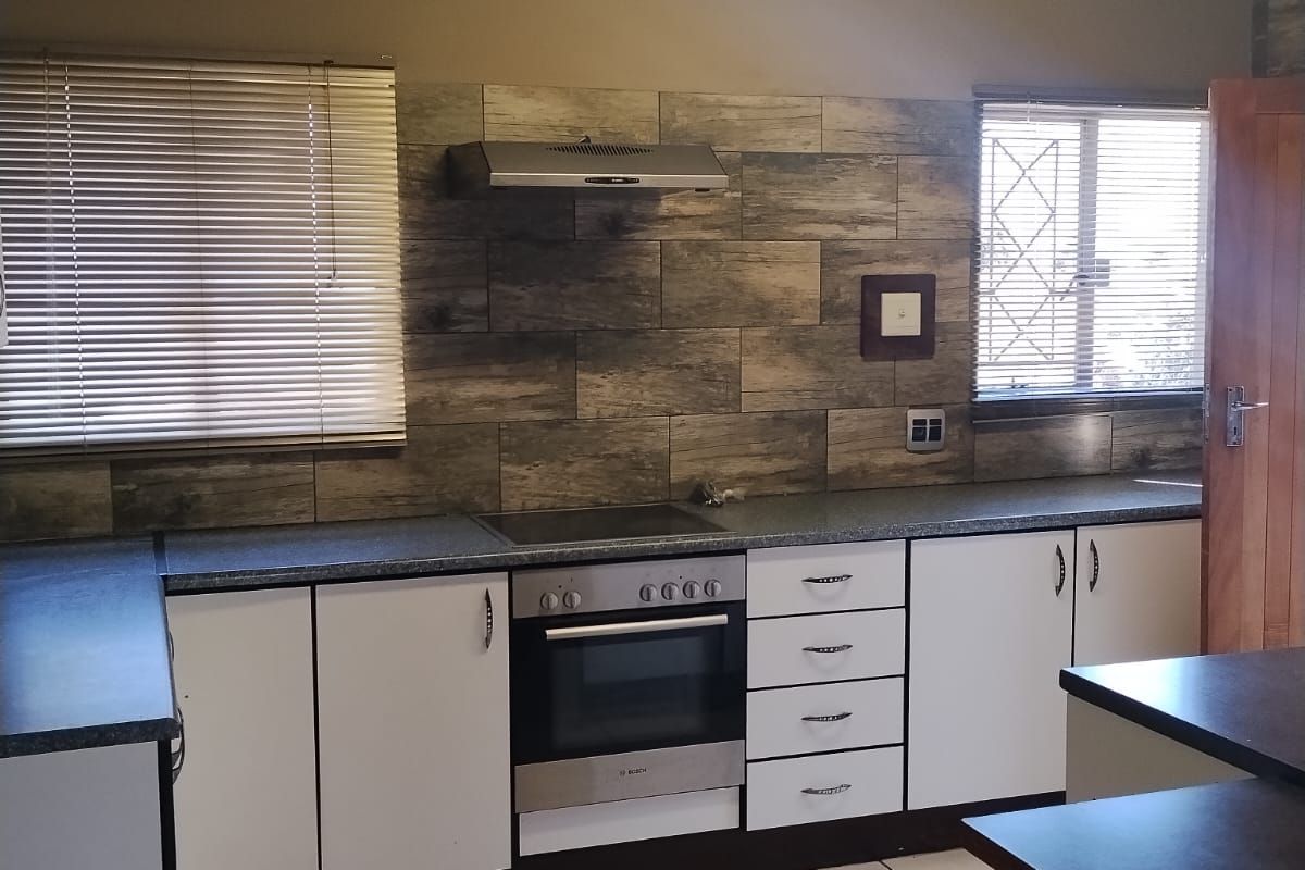 A functional kitchen featuring white cabinetry, a built-in oven with hob, tiled splashback, and timber ceiling finishes.