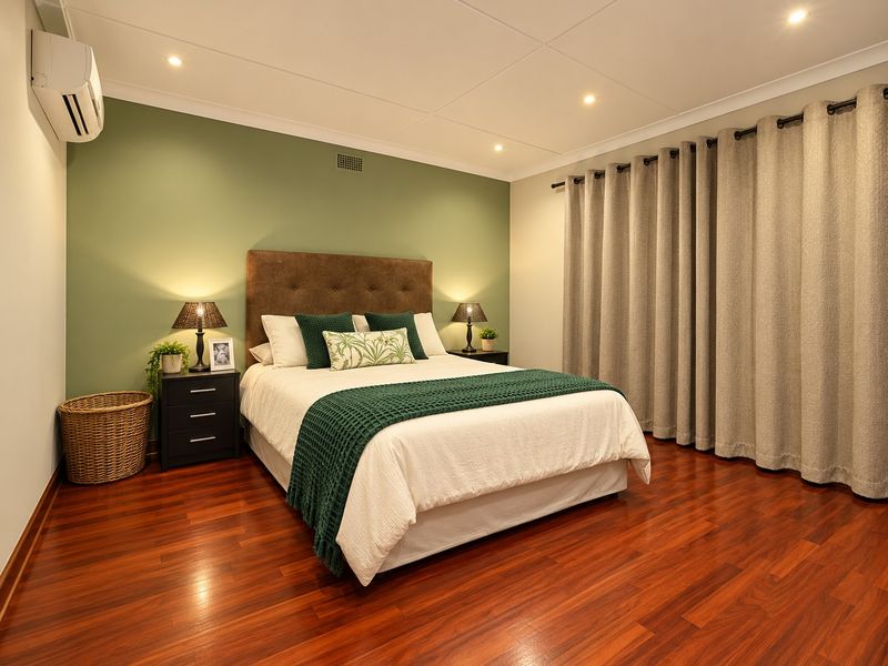 A well-maintained bedroom featuring polished hardwood flooring, a feature wall, recessed lighting, and a wall-mounted air conditioning unit.