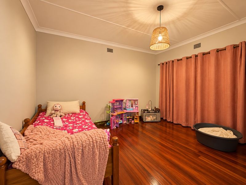 A spacious bedroom featuring polished hardwood flooring, neutral wall tones, and a decorative pendant light fixture, providing a comfortable and well-maintained living space.