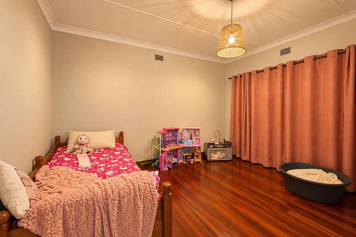 A spacious bedroom featuring polished hardwood flooring, neutral wall tones, and a decorative pendant light fixture, providing a comfortable and well-maintained living space.