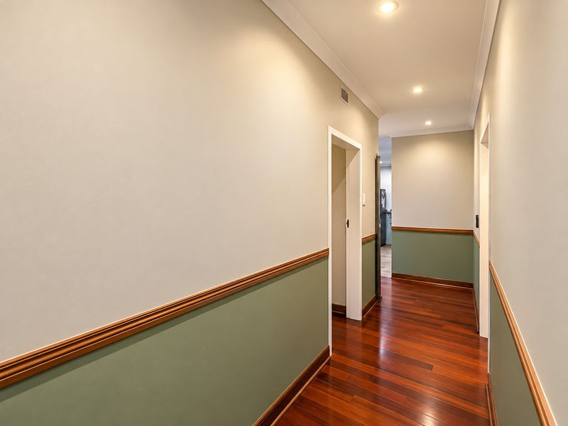 A clean and well-maintained hallway featuring polished timber flooring, two-tone wall paint with timber dado rail detailing, and recessed ceiling downlights.