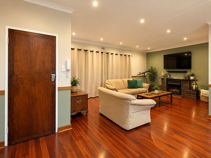 A well-maintained living room featuring polished timber flooring, a stone-clad fireplace, recessed downlighting, and a classic dado rail finish.