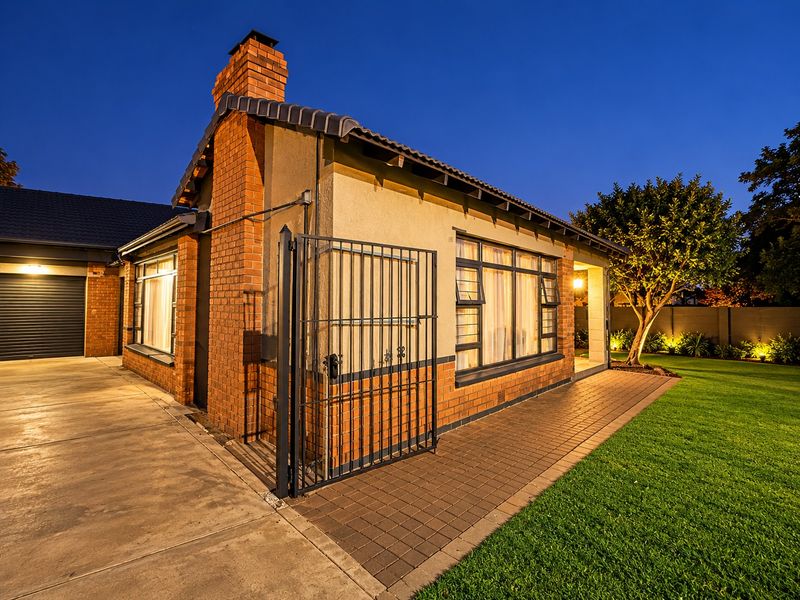 A well-maintained rear exterior view of the house featuring brick masonry, a paved walkway, a secure metal gate, and a manicured lawn at dusk.