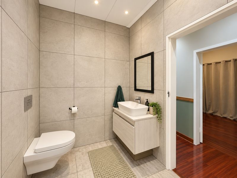 Modern bathroom featuring a wall-mounted toilet with concealed cistern, floating vanity with vessel sink, and contemporary large-format wall tiling.