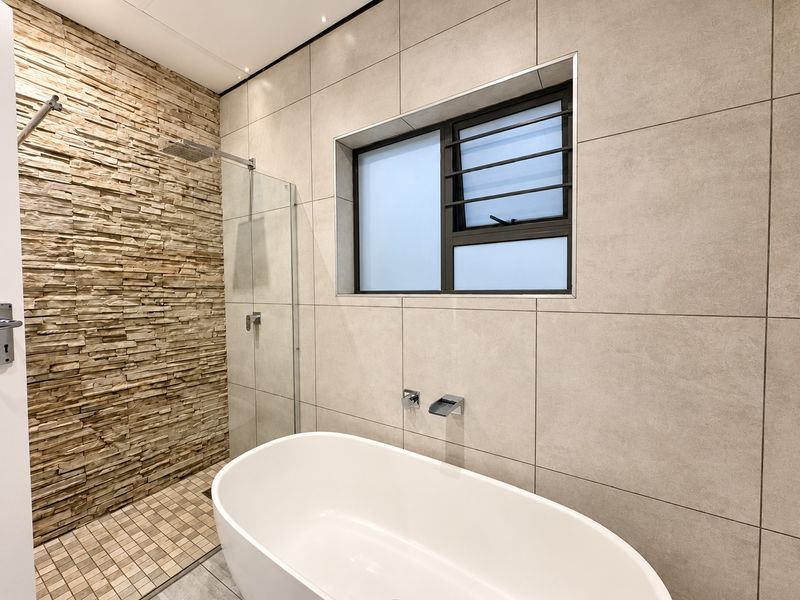 Modern bathroom featuring a freestanding bathtub, walk-in shower with stone cladding, and large format neutral wall tiles.