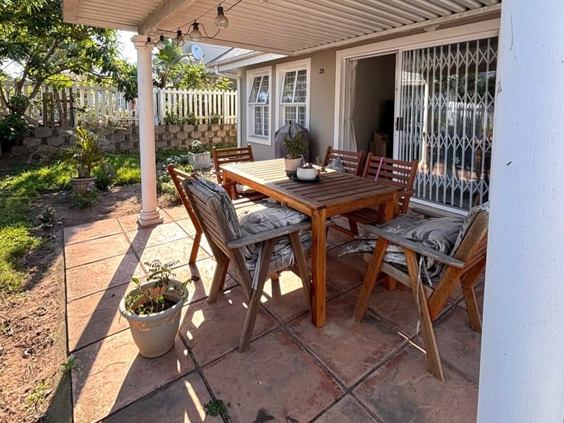 A covered outdoor patio area featuring paved flooring, providing direct access to the home through a sliding glass door with security gate.