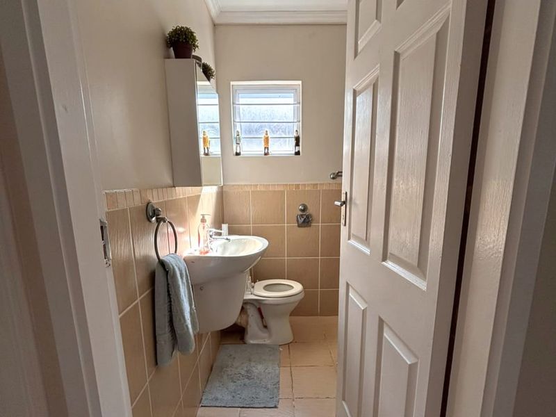 A compact bathroom featuring a pedestal washbasin, toilet, and neutral wall tiling, providing a functional and well-maintained space.